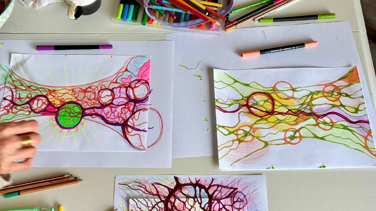 Overzicht van een wensboom-workshop met intuïtieve tekeningen in kleur, papier en stiften op tafel, terwijl deelnemers hun innerlijke proces zichtbaar maken door tekenen.